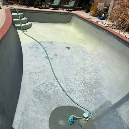 Drained pool with exposed waterline tile and a hose